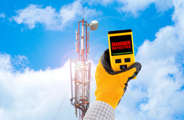 Handheld EMF meter beside a cellular tower against blue sky