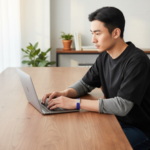 Asian man wearing blue EMF protection bracelet BodyBand Plus on MacBook