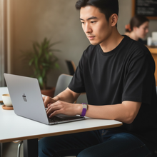 Asian man wearing purple EMF protection bracelet BodyBand Plus working on MacBook
