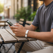 Man wearing white EMF protection bracelet BodyBand Plus using phone in park