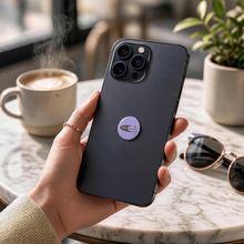 EMF Mini Shield – Glitz Cruzin Power Purple on the back of a smartphone, held in hand at a café — glitter purple EMF phone protection sticker