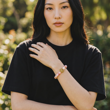 Woman wearing a pink beaded bracelet with gold dog paw charm and 240+ resonant frequencies for EMF protection.
