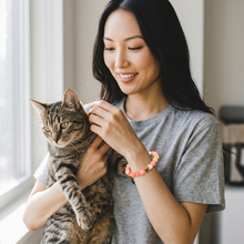 Woman holding her cat while wearing a Pink Cat Lover EMF Protection Bracelet designed for cat moms and pet lovers.