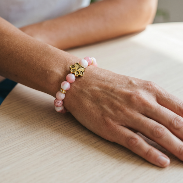 Close-up of a pink beaded EMF protection bracelet featuring a gold dog paw charm worn on the wrist.